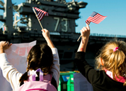 2 girls wave American flags at ship